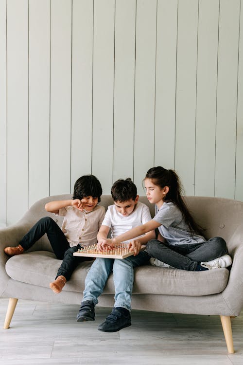 Children Sitting on a Couch Playing a Board Game