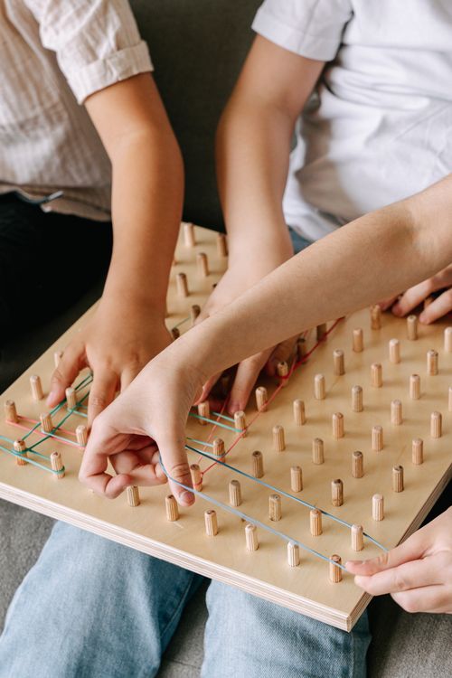 Free Children enjoy a mindful activity with a wooden geoboard, using colorful rubber bands. Stock Photo