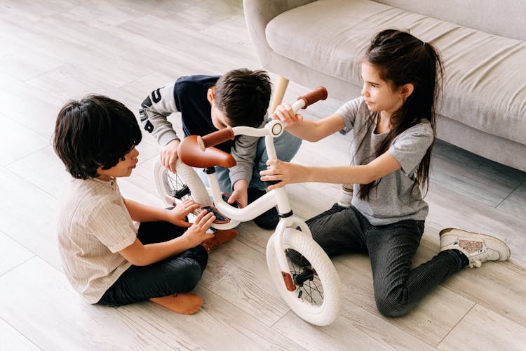 Kids Sitting On The Floor While Playing With A Bike