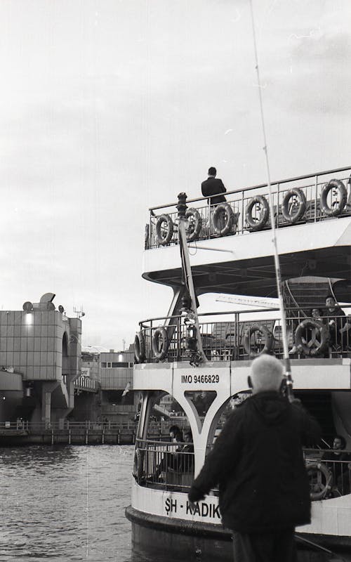 Grayscale Photo of Man Standing Near the Ferry
