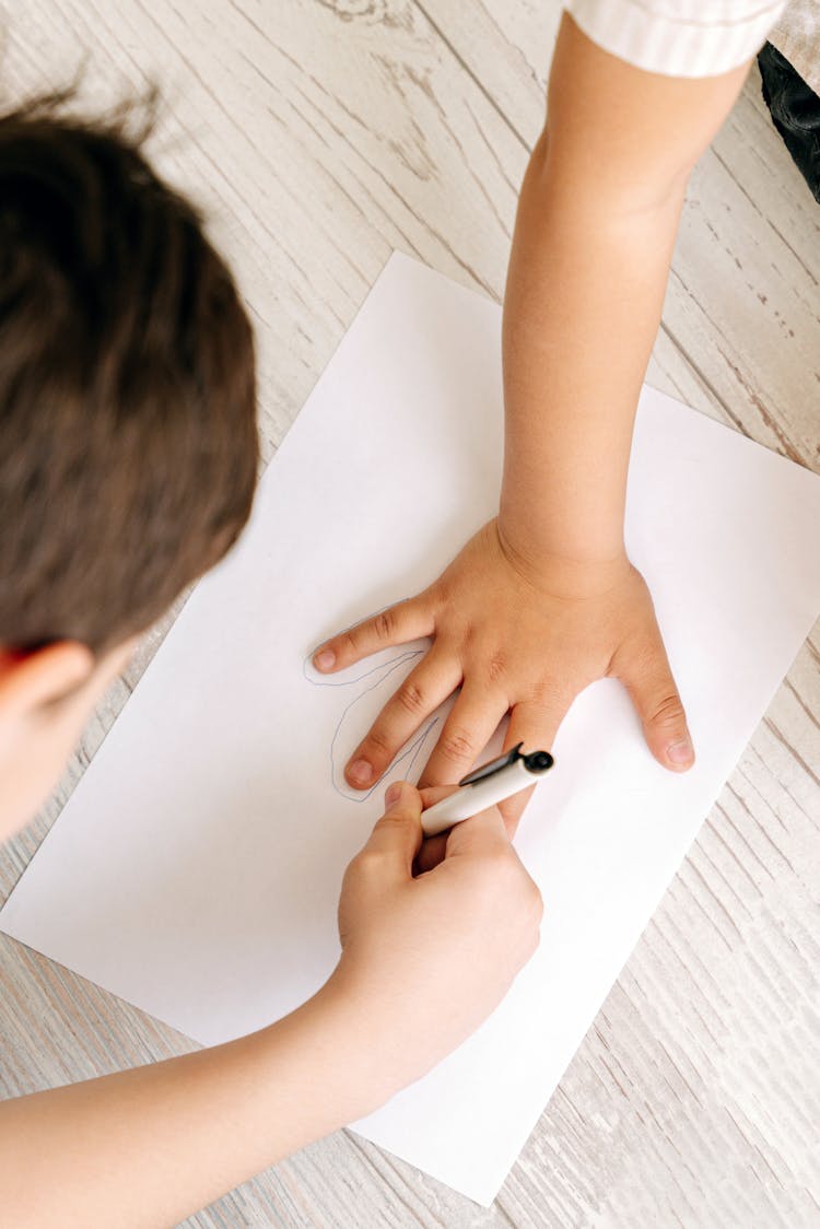 High-Angle Shot Of A Child Tracing Another Child's Hand On A Paper