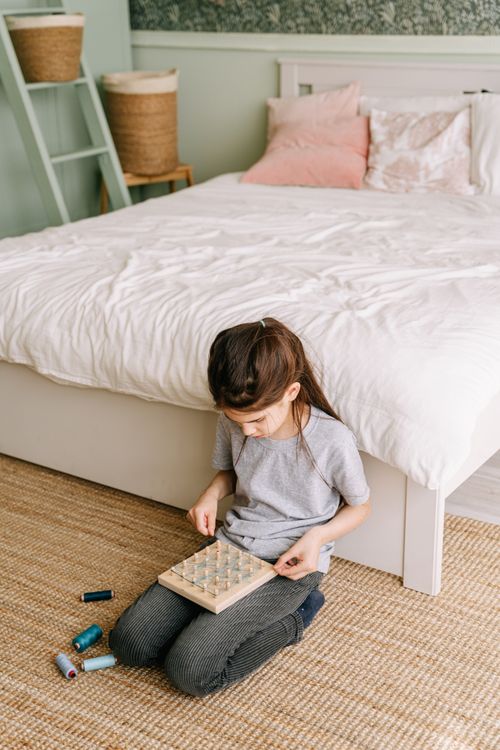 Free A young girl sitting in a cozy bedroom playing with a geoboard, emphasizing creativity and learning. Stock Photo