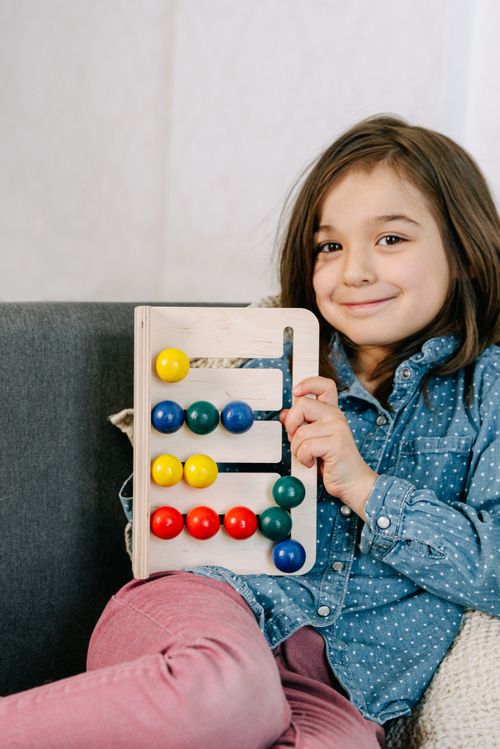 Free Young girl smiling while holding a colorful wooden abacus inside. Stock Photo