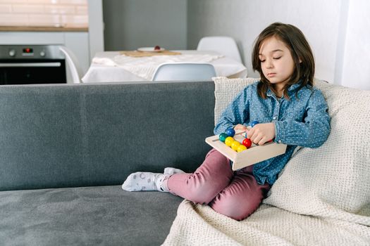 A Girl in Denim Jacket Sitting on the Couch while Holding a Wooden Toy