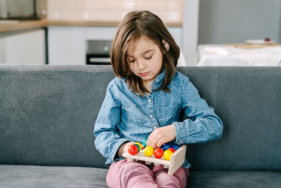 Photo by Ivan S on Pexels Kind im gepunkteten Hemd spielt mit Spielzeug auf einem Sofa und legt dabei Wert auf Freizeit und Lernen. - Foto von Ivan S auf Pexels