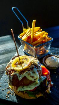 Close-up of a gourmet burger and fries, beautifully plated on a wooden tray under dramatic lighting.