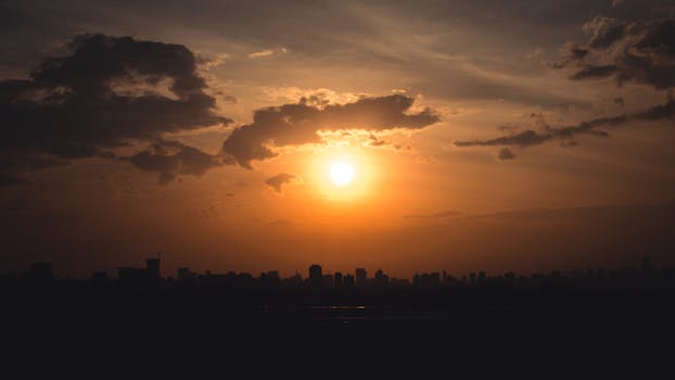 Beautiful urban skyline silhouette during sunset with dramatic clouds and golden hues.