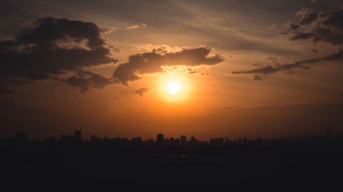 Free Beautiful urban skyline silhouette during sunset with dramatic clouds and golden hues. Stock Photo
