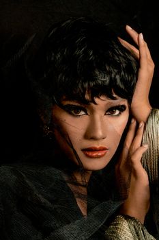 A striking portrait of a woman with bold eye makeup and a captivating gaze, draped in fine mesh.