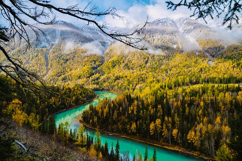 Free Serene river winding through vibrant autumn forest and majestic mountains. Stock Photo