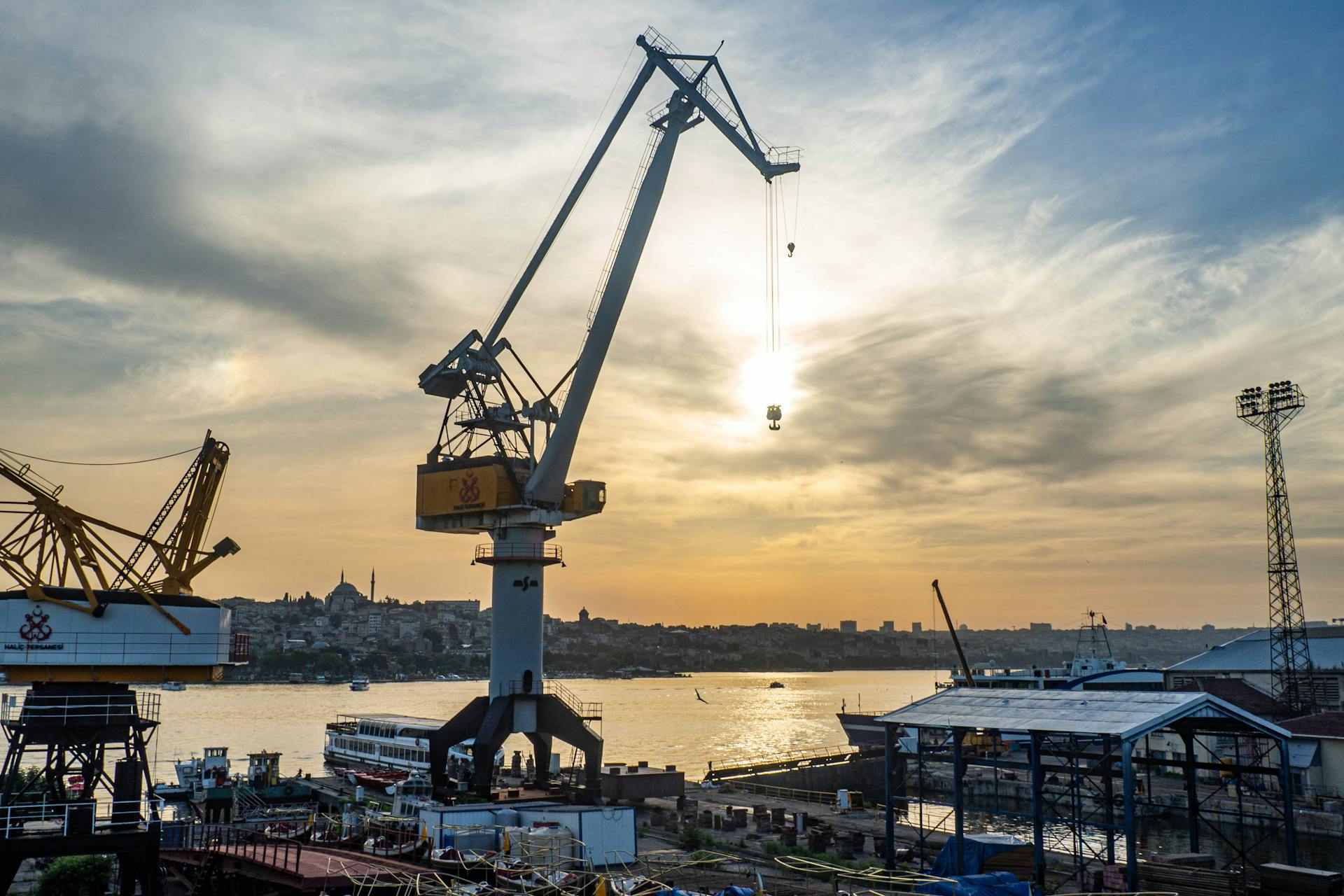 A scenic view of construction cranes at a harbor during sunset, overlooking the waterfront cityscape.