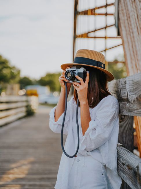 Young woman in a hat taking photos outdoors with a vintage camera, capturing a sunny day.