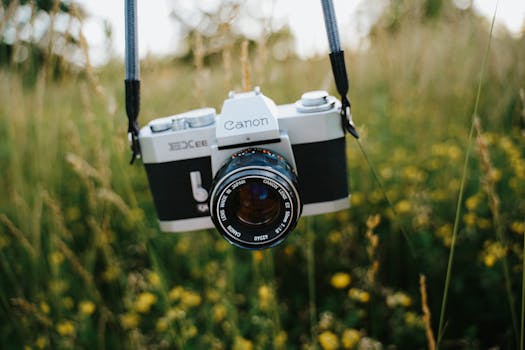 A classic camera with a lens, hanging outdoors in a field of grass and flowers.
