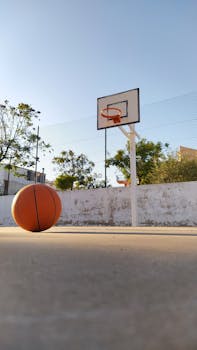 A sunny outdoor basketball court in Faro, Portugal with a hoop and basketball.