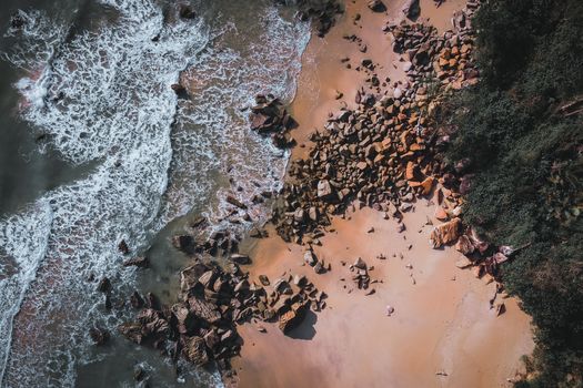 Drone shot capturing waves crashing onto a rocky shoreline with sandy beach.