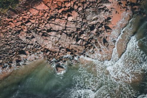 Free A mesmerizing aerial shot capturing rocky shores with waves crashing at the coastline. Stock Photo