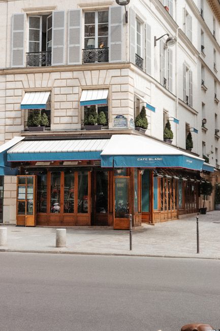 Exterior of a classic Parisian cafe with blue canopy on a sunny day.