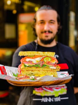 Close-up of a gourmet burger held by a bearded chef, emphasizing fresh ingredients and culinary artistry.