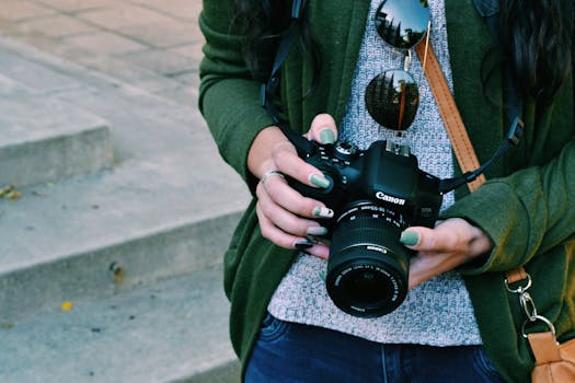 A woman with manicured nails holds a DSLR camera in an outdoor setting.
