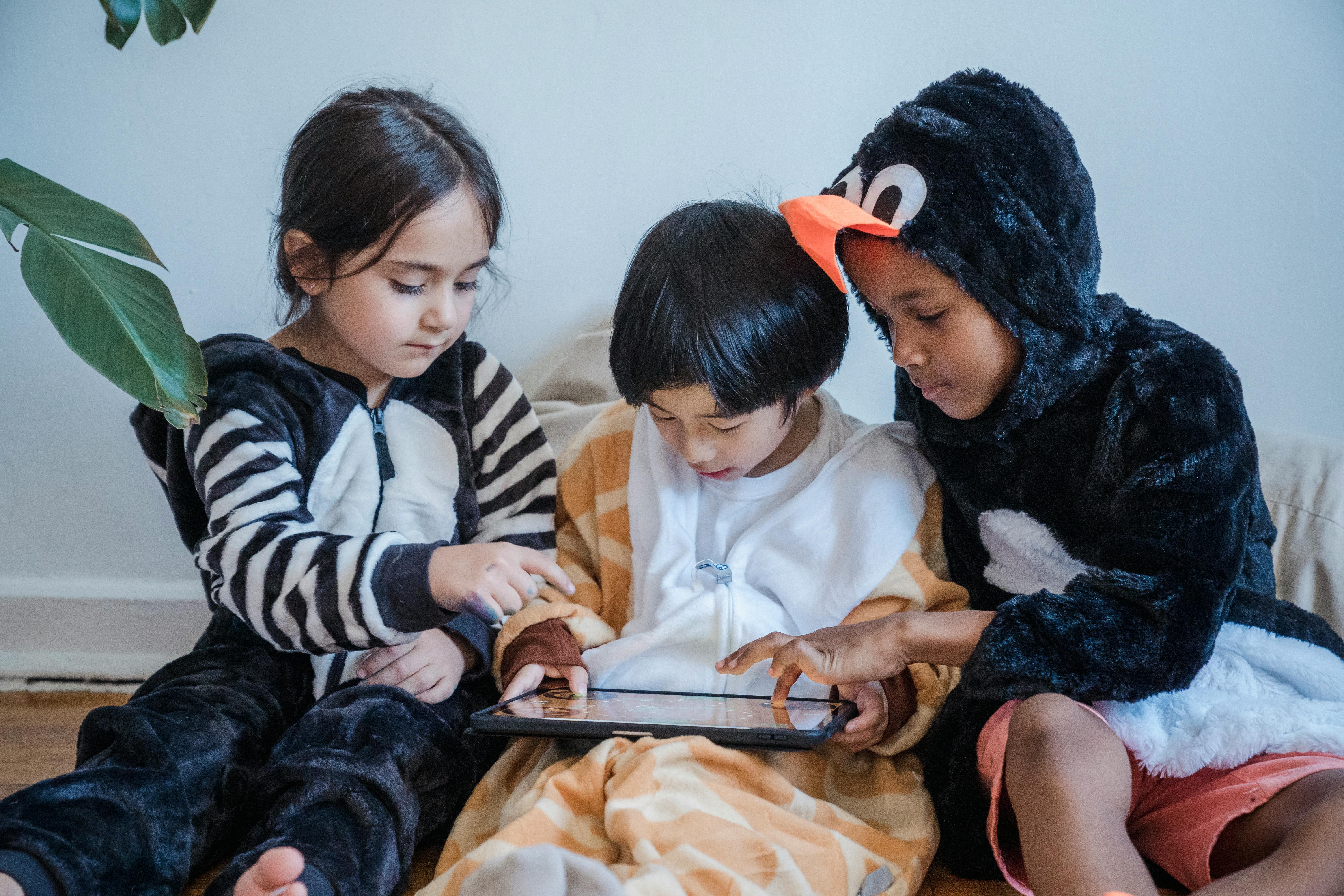 kids in costumes playing games with tablet computer