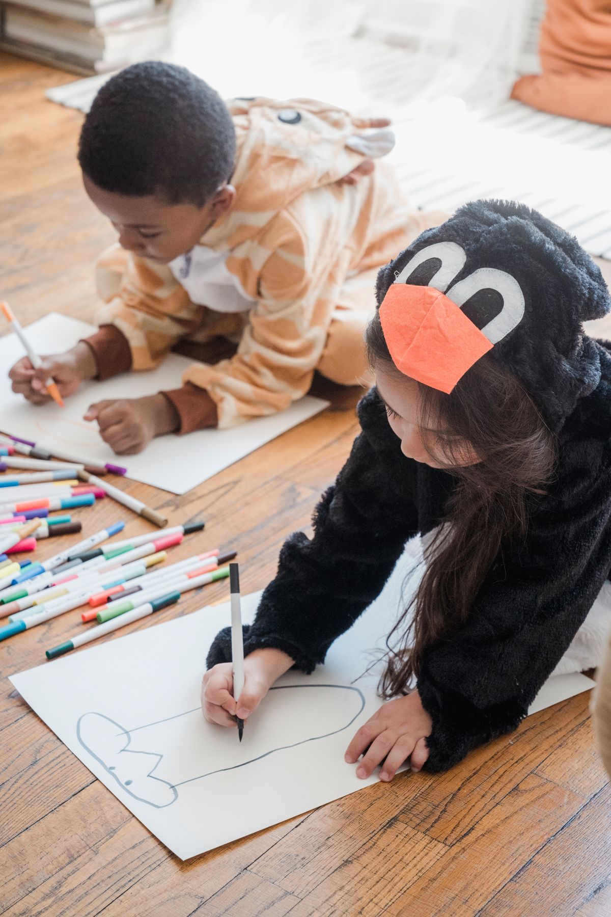 Two kids in animal costumes drawing colorful pictures of a sheep on white paper