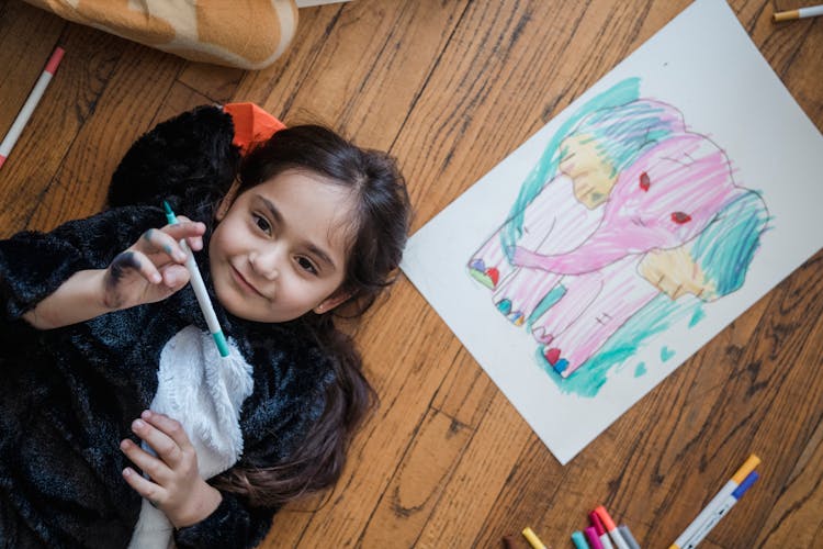 Little Girl Lying On Ground Next To Marker Drawing