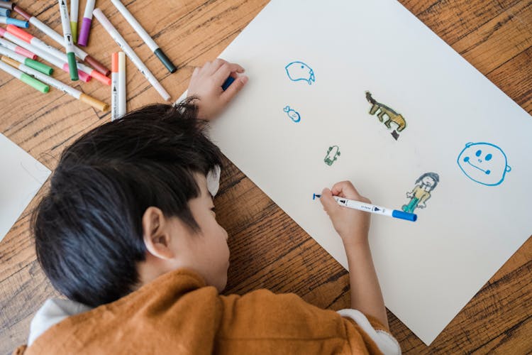 A Kid In Brown Hoodie Drawing On A White Paper