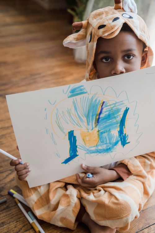 Free Adorable child in a giraffe onesie showing off their colorful drawing indoors. Stock Photo