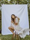 Woman in White Dress with Hat on Her Back Sitting on Chair Near White Textile Background