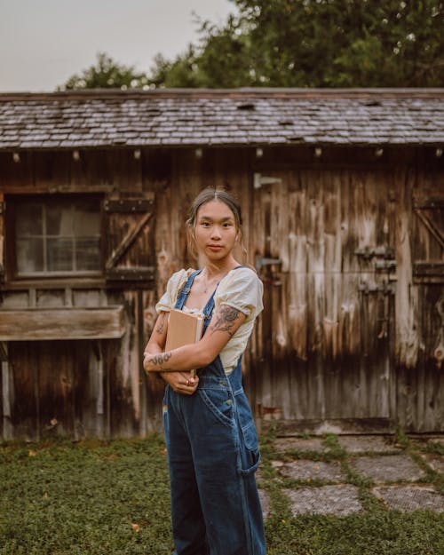 A Woman in Denim Jumper Standing Near the Wooden House
