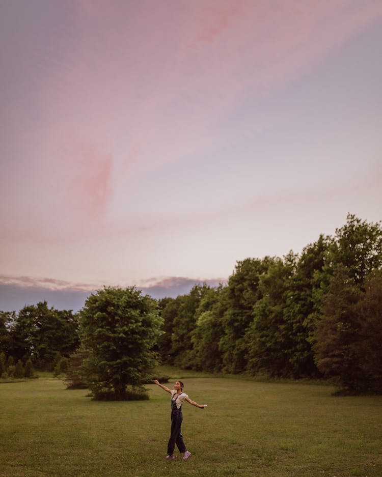 Girl In Denim Overall Standing On Green Grass Field During Sunset