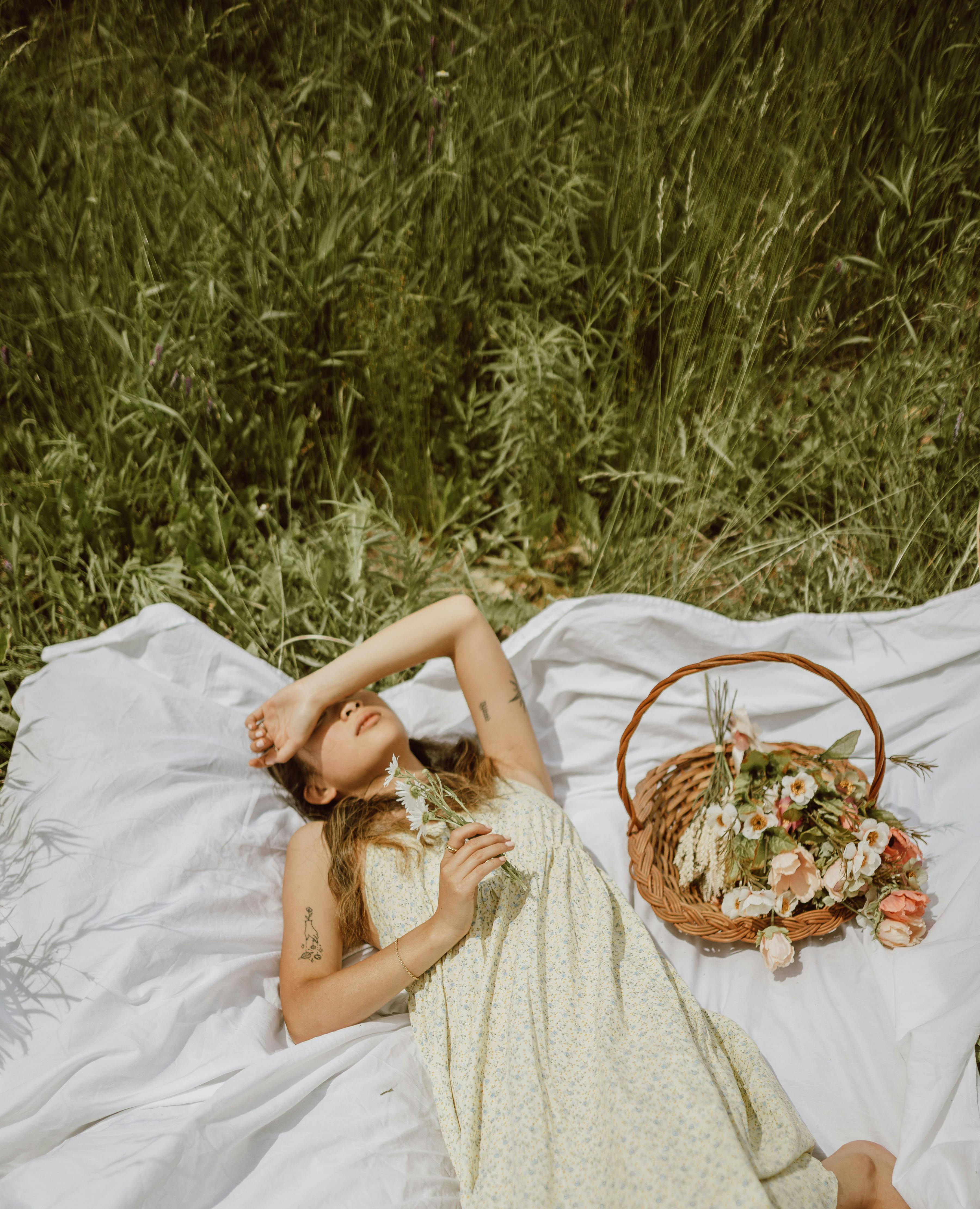 A woman lies on a blanket with a flower basket in sunny grassland, evoking relaxation.