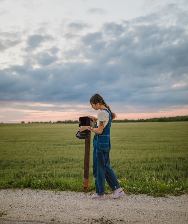 A Woman In Overalls Looking At A Mailbox 