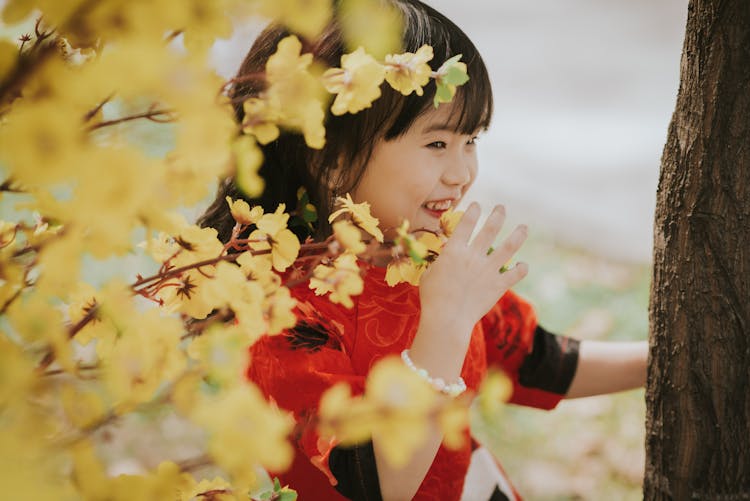 Laughing Little Girl Hiding Behind Bush Of Yellow Flowers