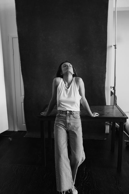 Monochrome portrait of a woman in casual denim attire leaning on a table, evoking a relaxed and thoughtful mood.