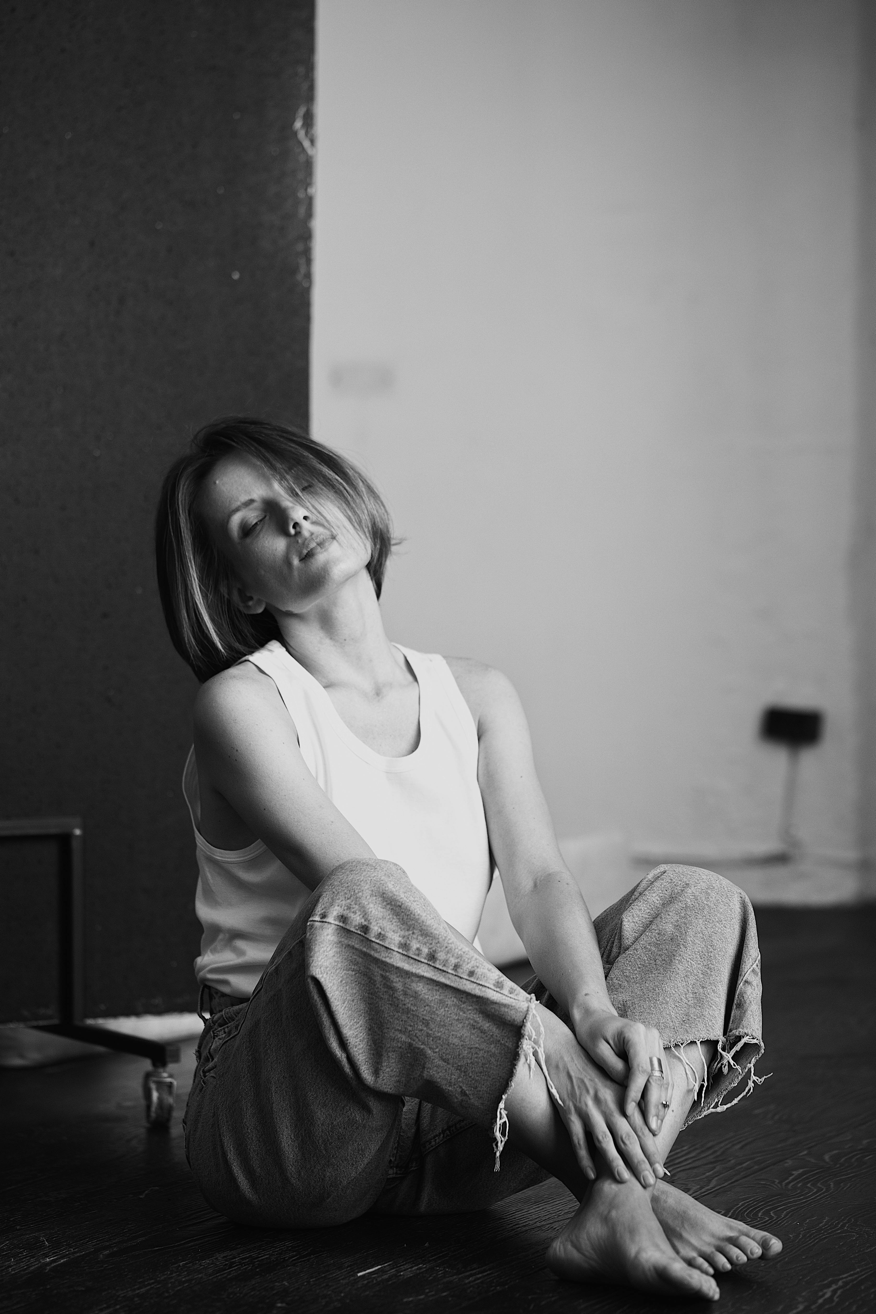 Black and white portrait of a woman sitting with eyes closed in a minimalist setting.