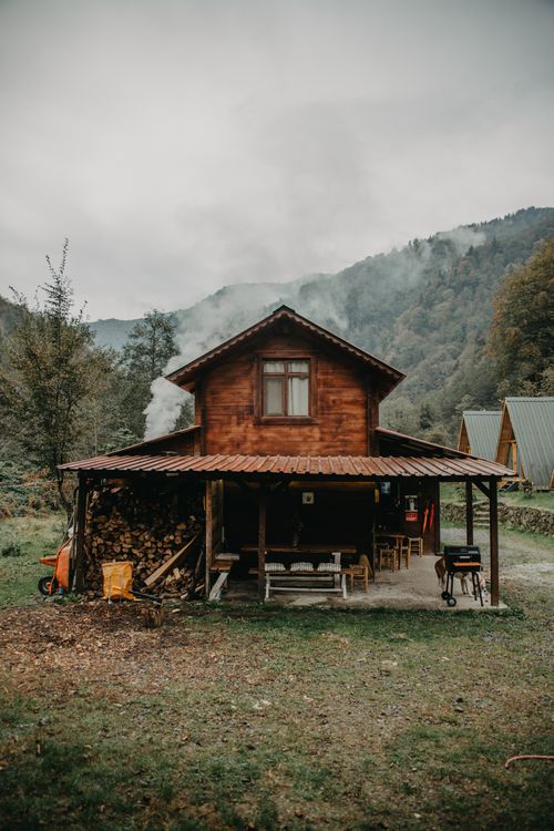 Free A rustic wooden cabin with smoke rising from the chimney in a serene forest setting, ideal for nature lovers. Stock Photo