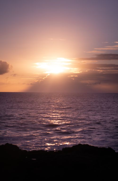 Free A tranquil seascape featuring the setting sun casting a warm glow on calm ocean waters. Stock Photo