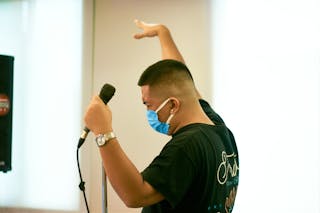 Man in Black T-shirt Wearing Face Mask While Holding Microphone and Raising Hand Up