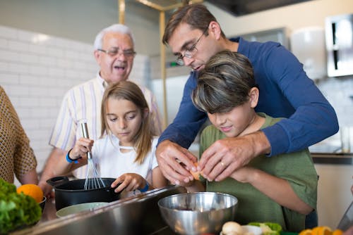 Free Man in Blue Sweater Assisting the Boy in Green Shirt Cracking Eggs Stock Photo