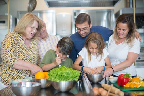 Girl Cracking Egg on a Stainless Bowl with Family beside her