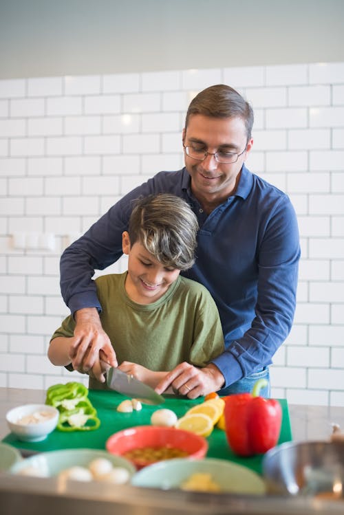 Free Man in Blue Long Sleeve Shirt Assisting the Boy to Use the Knife Stock Photo