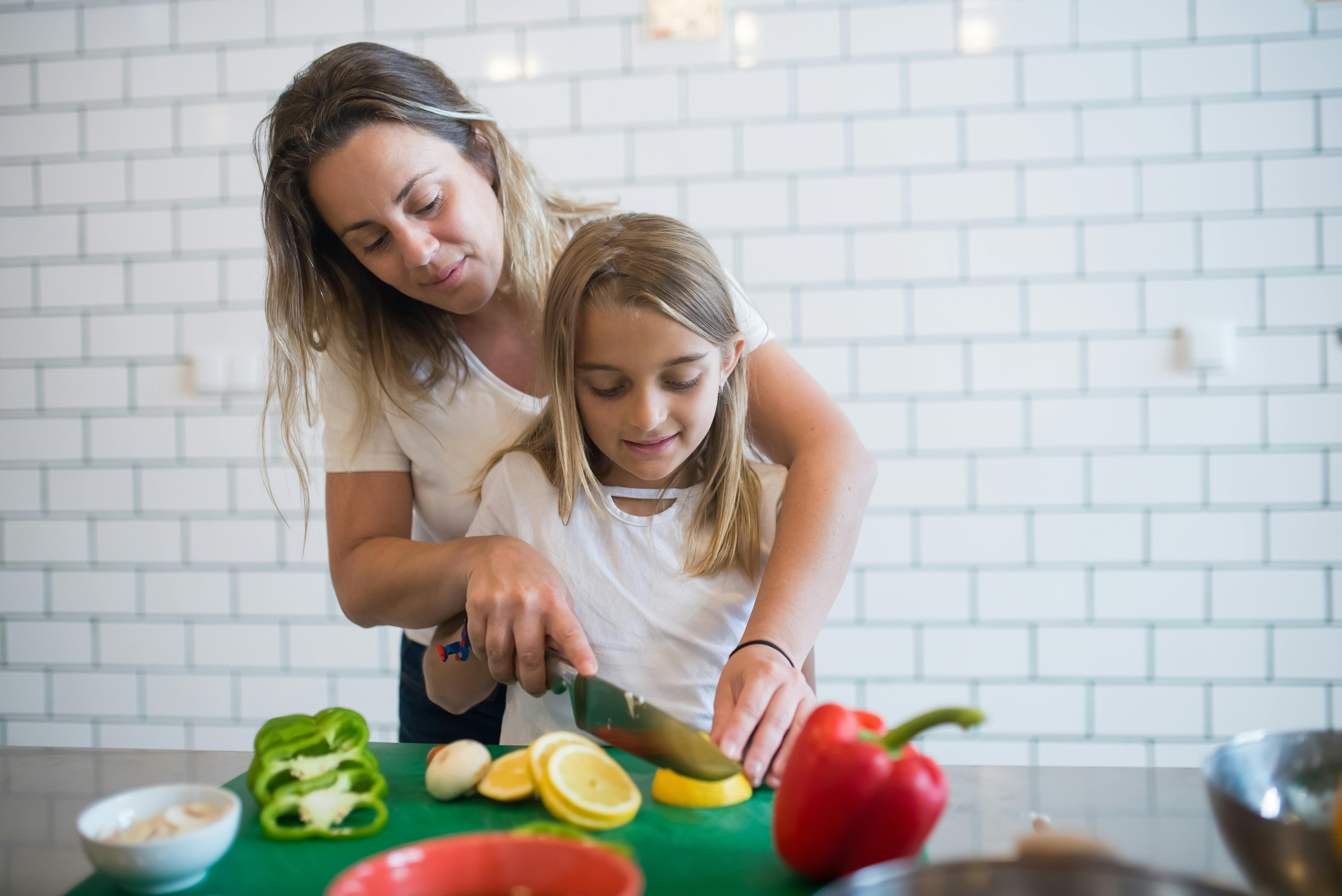 girl in white tank top assisting daughter to chop lemon