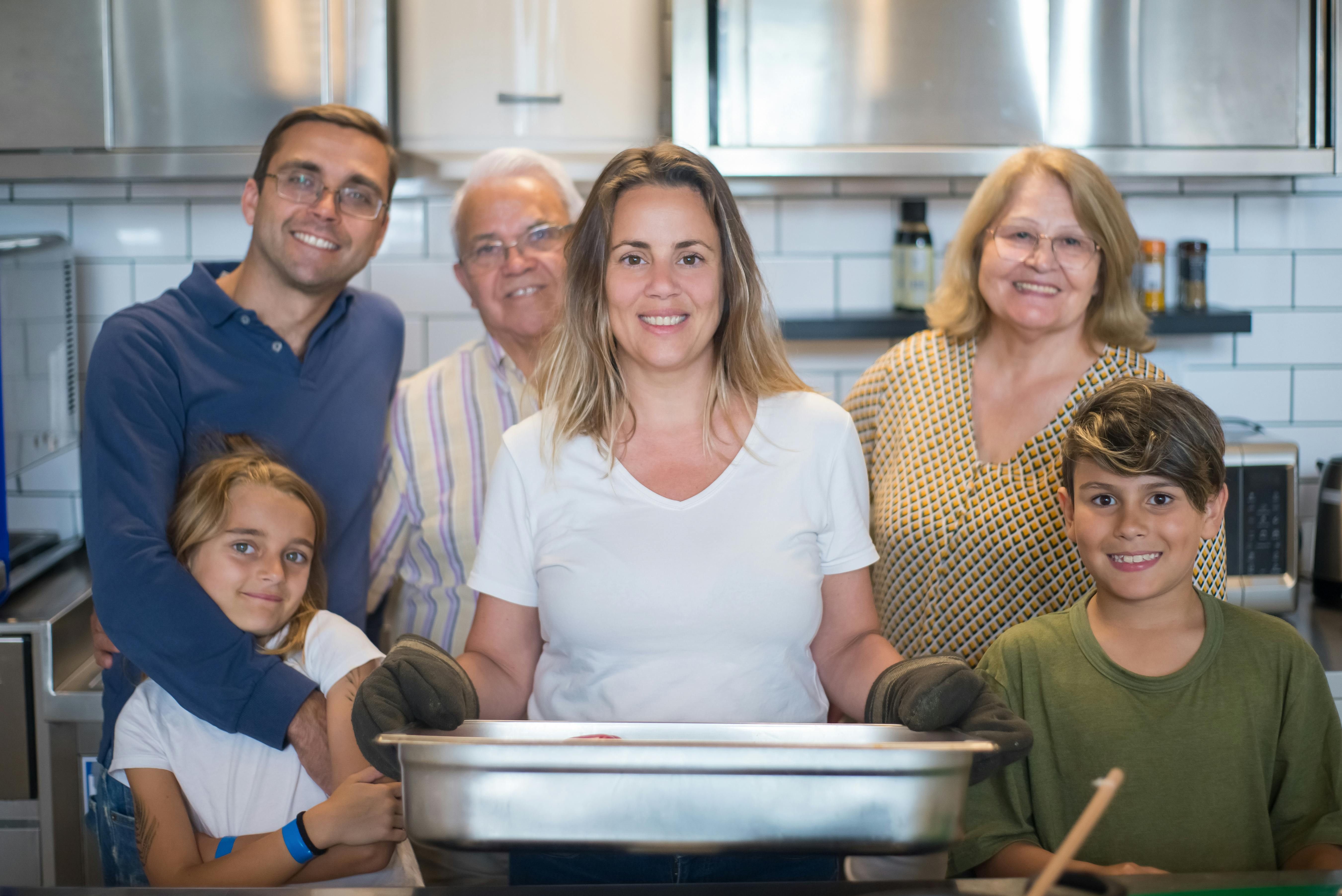 a woman in white shirt smiling while holding a stainless tray near her family