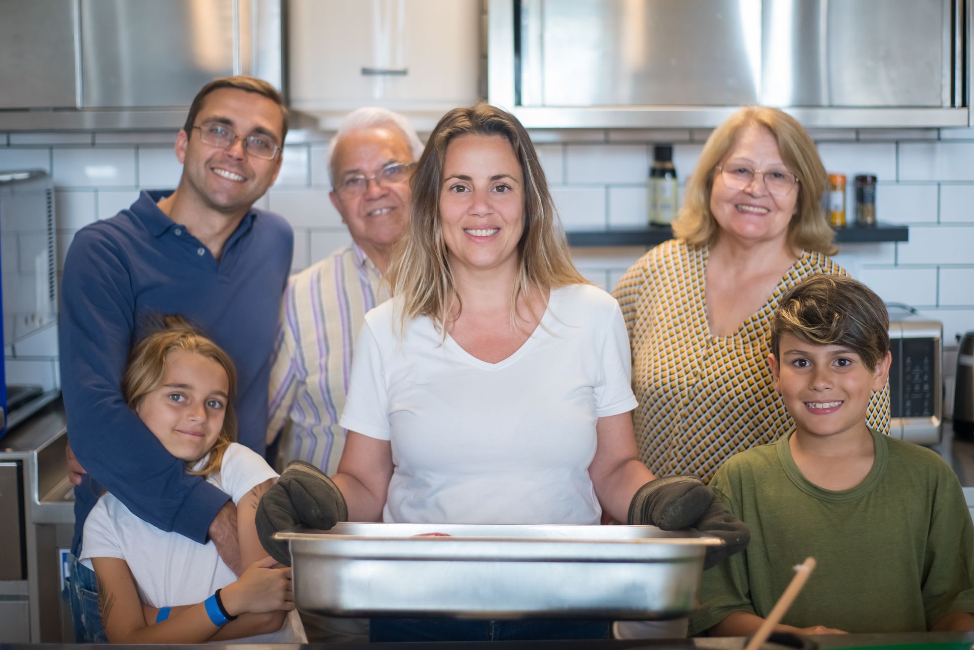A Woman in White Shirt Smiling while Holding a Stainless Tray Near Her Family