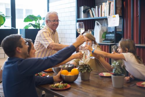 Free A multigenerational family raising glasses in a joyous toast at a kitchen table during a meal. Stock Photo