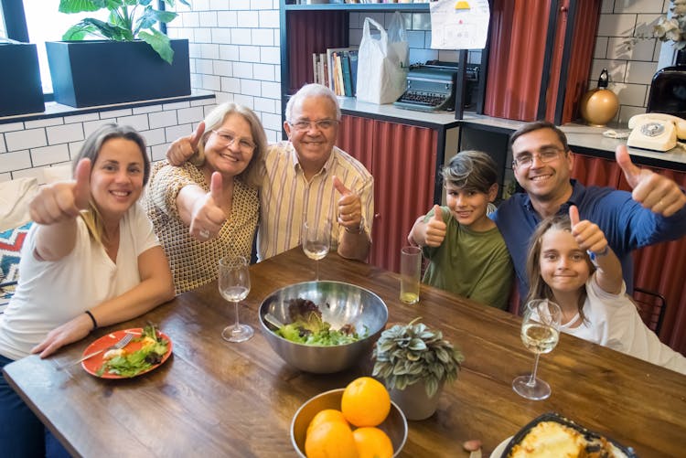 Family Sitting At Table And Showing Thumbs Up