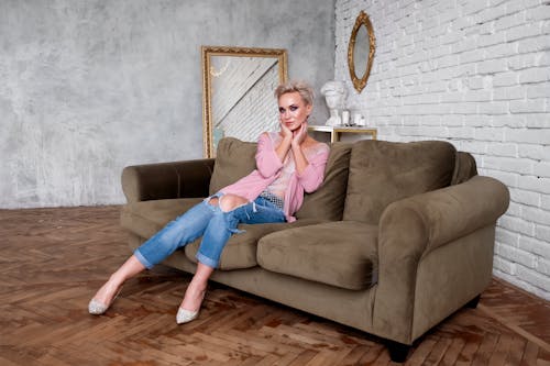 Woman in Pink Jacket and Blue Denim Jeans Sitting on Brown Sofa