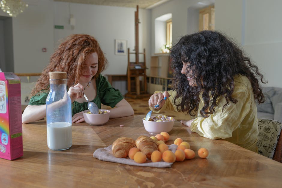 best willis tx registered nurse - Two young women enjoying breakfast at home with cereal, croissants, and fruit around a wooden table.