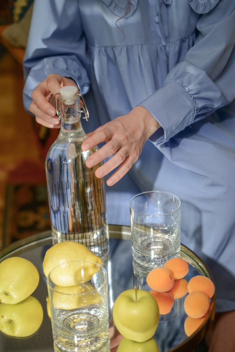 A Person In Blue Dress Opening The Cap Of The Glass Bottle On The Table